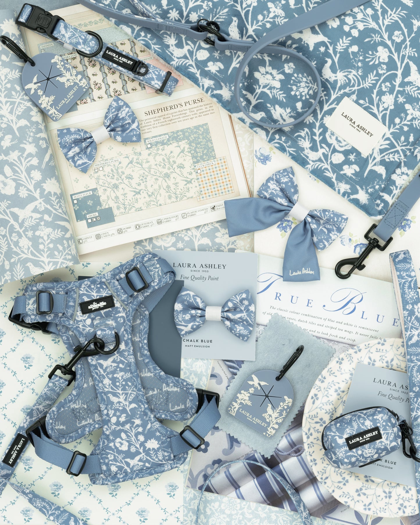 Collection of blue and white floral pet accessories including a harness, lead, collar and bow ties on a floral patterned background.