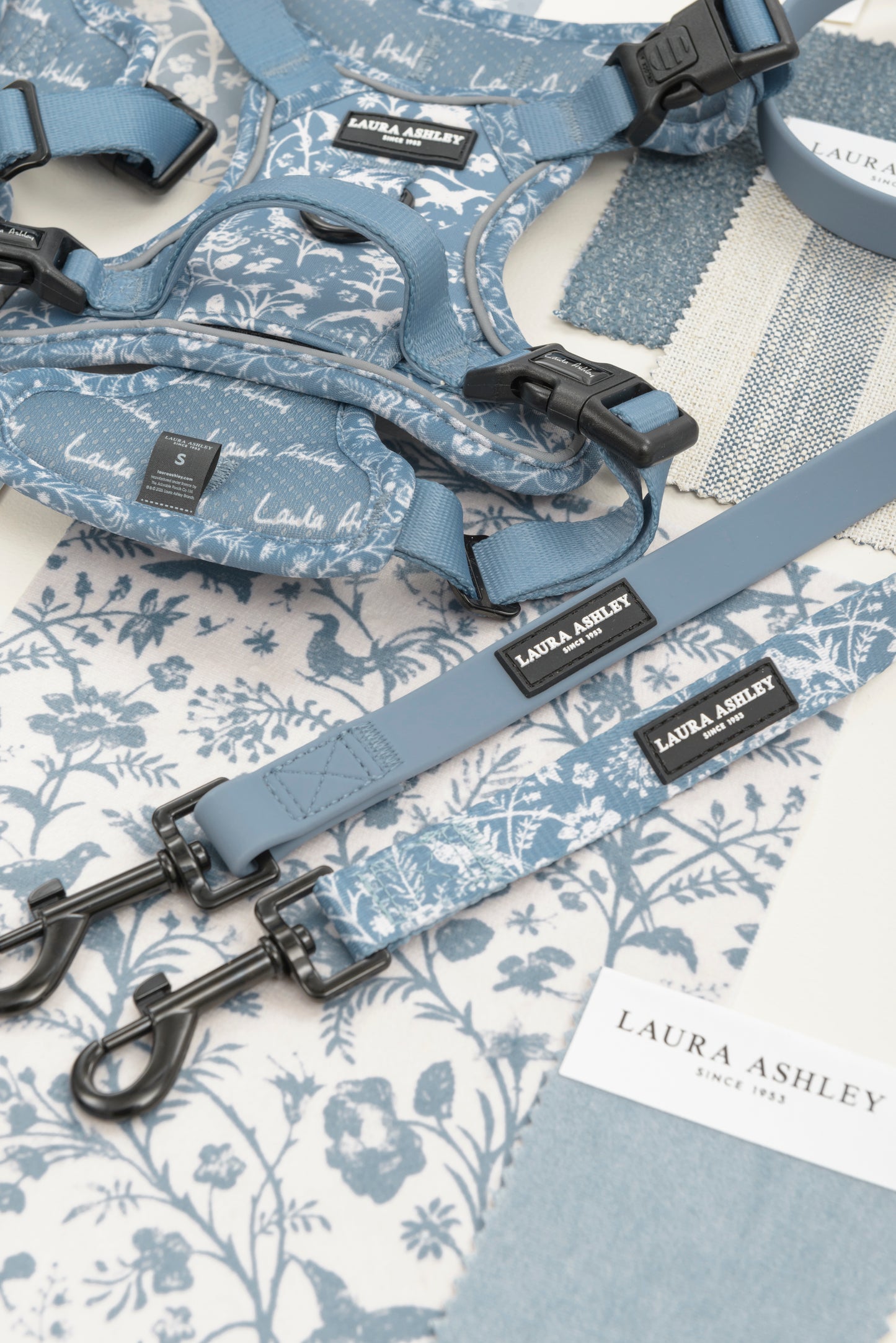 Dog harness and leads with blue and white Shepherd's Purse floral pattern on a matching fabric background, featuring Laura Ashley branding and black hardware.