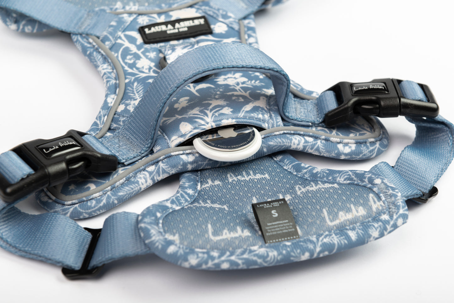 Blue floral-patterned dog harness with black hardware on a white background. Apple AirTag positioned in patented air pouch pocket for demonstration
