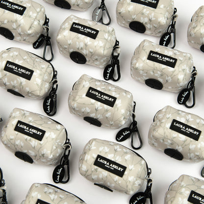 Magnolia Grove fabric dog waste bag dispenser in cream and white floral pattern with Laura Ashley label and hardware on a white background.